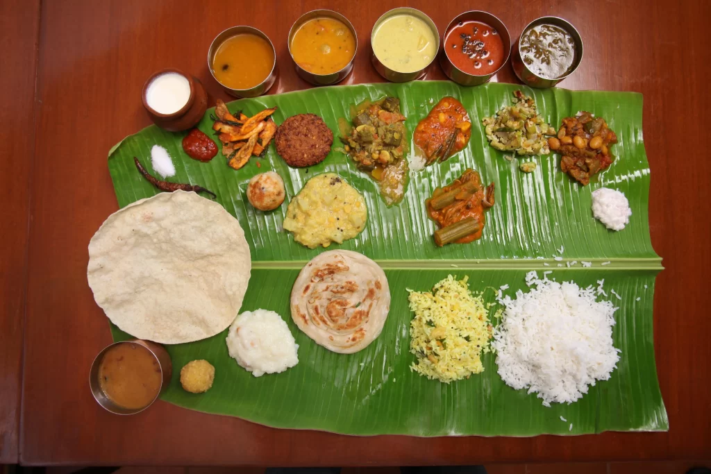 South Indian Wedding Catering Cost in London: Complete 2026 Pricing Guide 3 Traditional South Indian vegetarian feast arranged on a banana leaf, with white rice, lemon rice, parotta, papad, assorted vegetable curries, chutneys, pickles, sauces, and beverages served in small bowls.